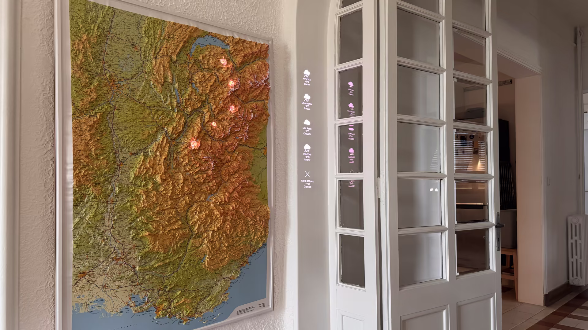 A large 3D map hung on a wall, with ski stations highlighted by the Lightbulb Computer and their respective weather conditions projected next to the map