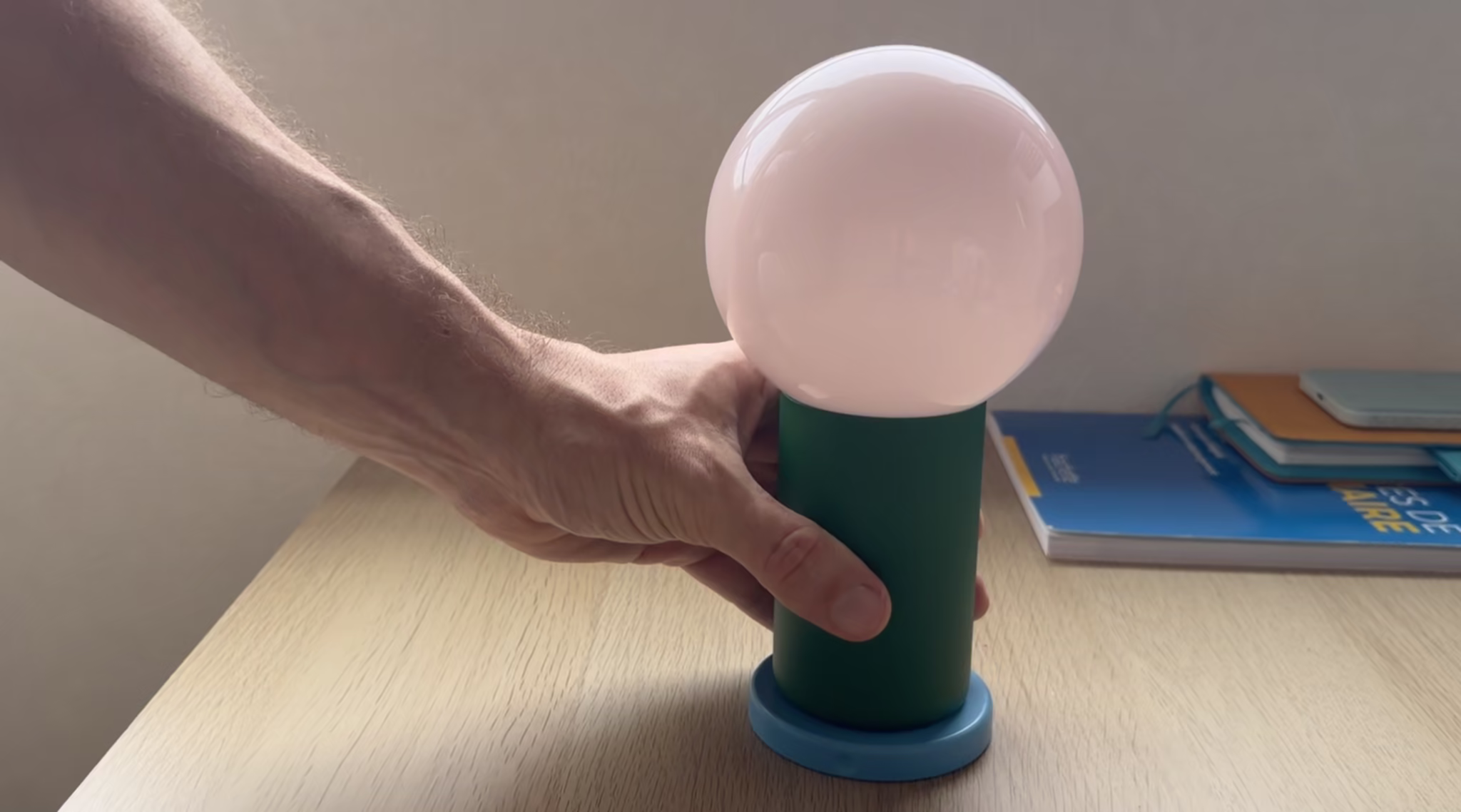 A hand placing down a cylindrical base on top of which a large lightbulb is screwed in.